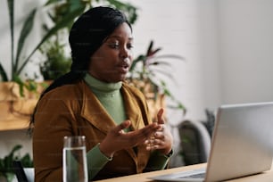 Giovane psicoanalista afroamericano fiducioso seduto alla scrivania davanti al computer portatile e che parla con il paziente durante la sessione psicologica online