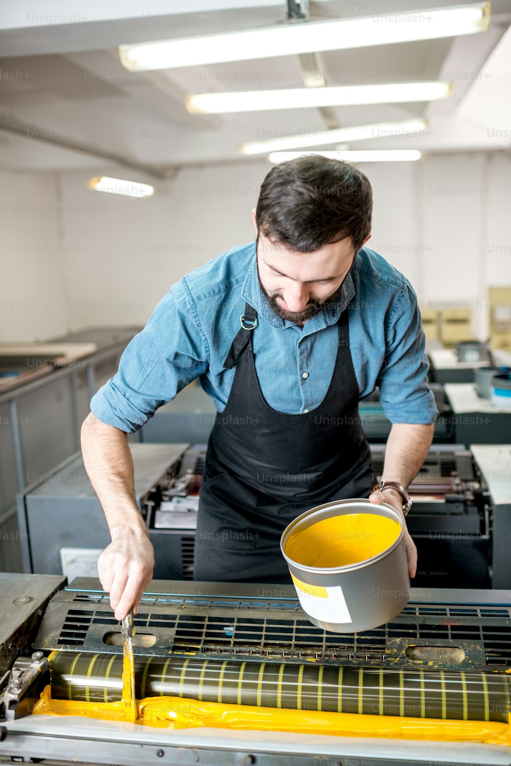 Tipógrafo rellenando pintura amarilla en la máquina offset en la fabricación de impresión