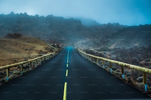 foggy and misty road with yellow line in the middle. clouds on mountains invade the asphalt. misterious scene.