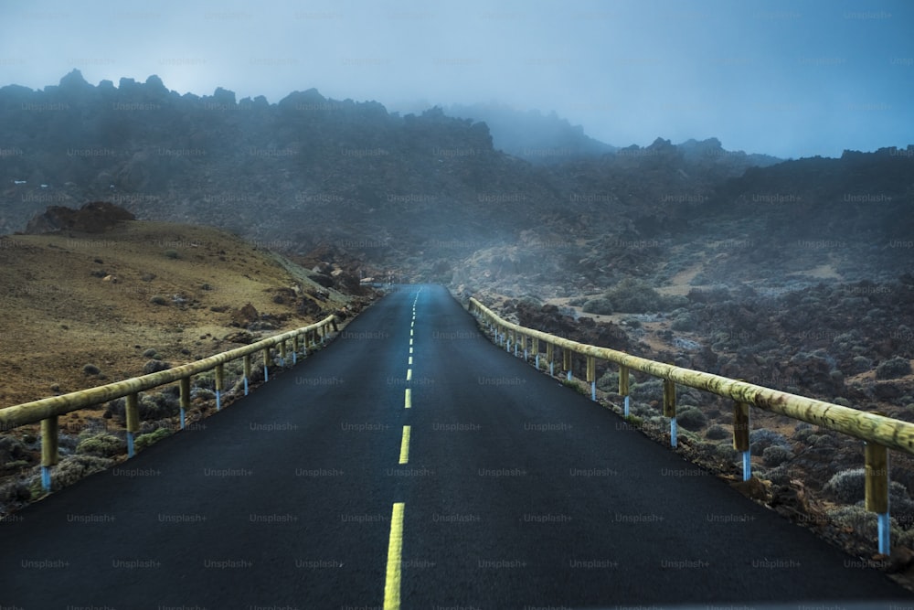 Carretera brumosa y brumosa con línea amarilla en el medio. Las nubes en las montañas invaden el asfalto. Escena misteriosa.