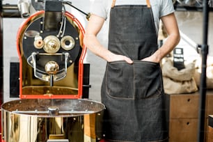 Barista in apron with hands in the pockets standing near the roaster machine