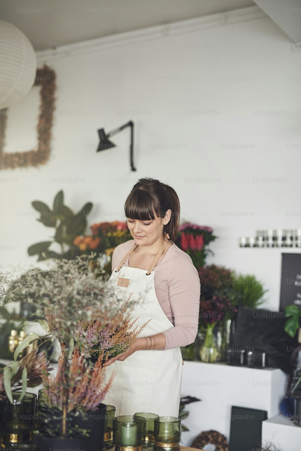 Young female florist arranging potted plants on a display table while busy working in her flower shop