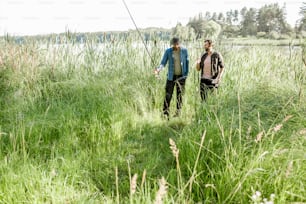 朝、湖畔の緑の芝生を釣り竿と網を持って歩く2人の漁師