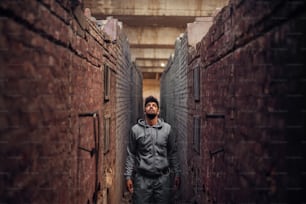 Portrait d’un jeune homme sportif afro-américain concentré et motivé avec des écouteurs, debout à l’intérieur de l’endroit abandonné au milieu de deux murs et réfléchissant en regardant vers le haut.