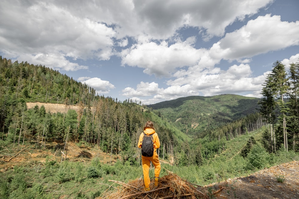 Une personne en combinaison de sport orange et un sac à dos profite d’une vue magnifique sur les montagnes, voyageant dans la nature en été.