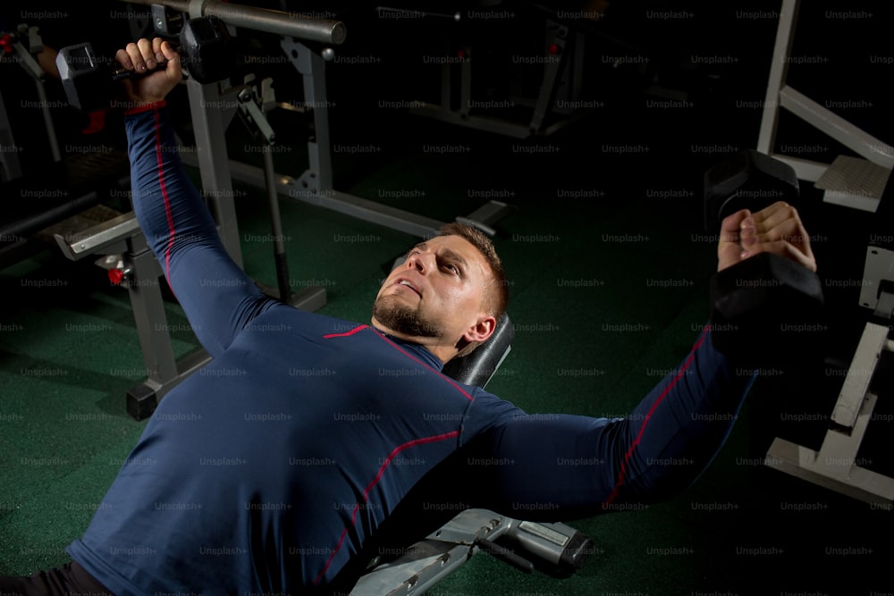 Young man pumping his arm muscles with barbells in gym