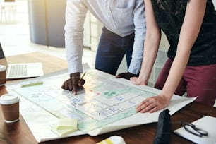 Two architects standing together in a modern office leaning over a desk discussing a building design