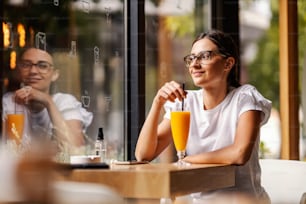 Ein fröhliches College-Mädchen, das in ihrer Pause in der Cafeteria sitzt und frischen Orangensaft trinkt. Es ist wichtig, genügend Vitamine zu haben