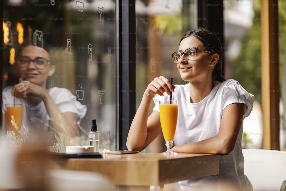 Ein fröhliches College-Mädchen, das in ihrer Pause in der Cafeteria sitzt und frischen Orangensaft trinkt. Es ist wichtig, genügend Vitamine zu haben