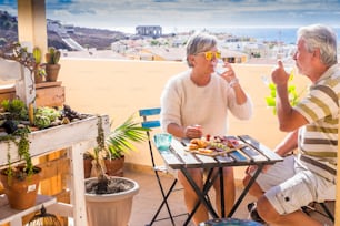 Coppia adulta anziana caucasica mangia e si gode il tempo libero all'aperto insieme mangiando e bevendo una colazione in una mattina soleggiata sul tetto con vista sull'oceano. concetto di vacanza e pensionato