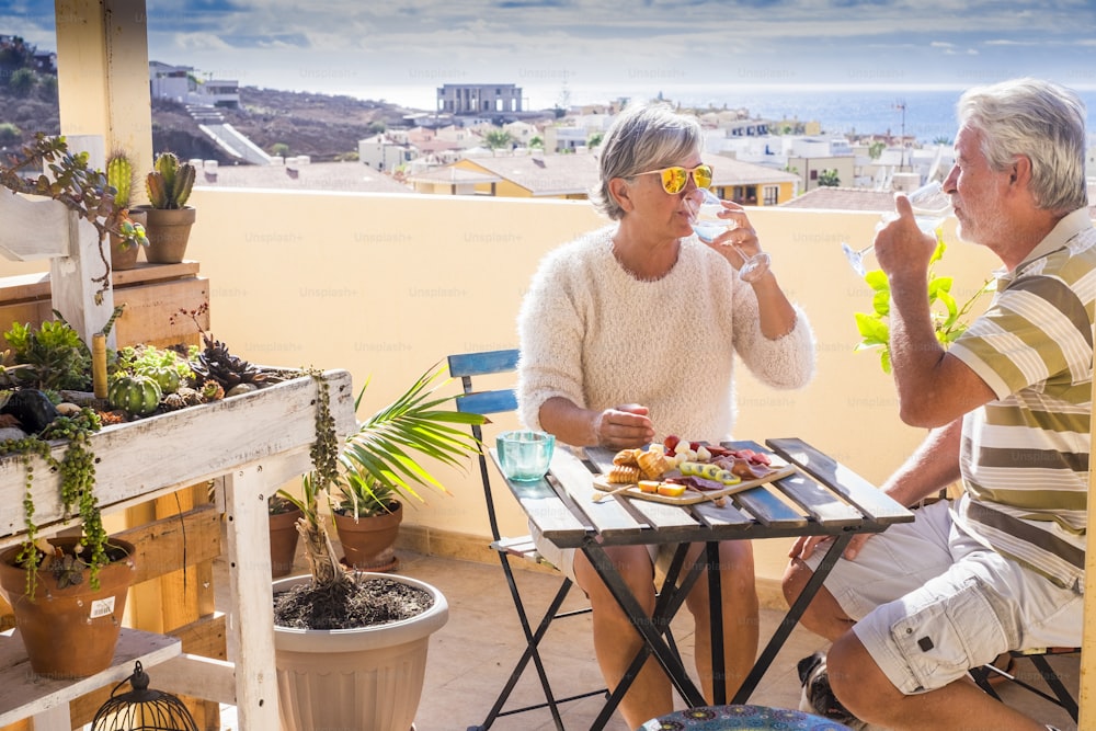 caucasian senior adult couple eat and enjoy leisure outdoor together eating and drinking a breakfast in a sunny morning on the rooftop with ocean view. vacation and retired concept