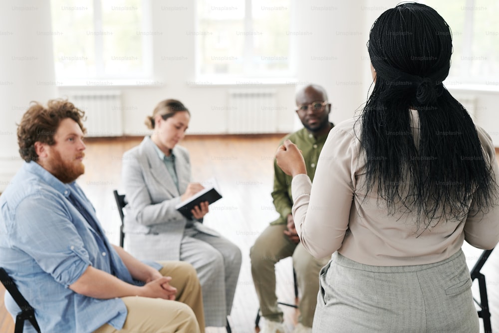 심리학 세션의 과정에 참석하는 환자 그룹 앞에 서서 자신의 문제를 설명하는 흑인 여성의 뒷모습