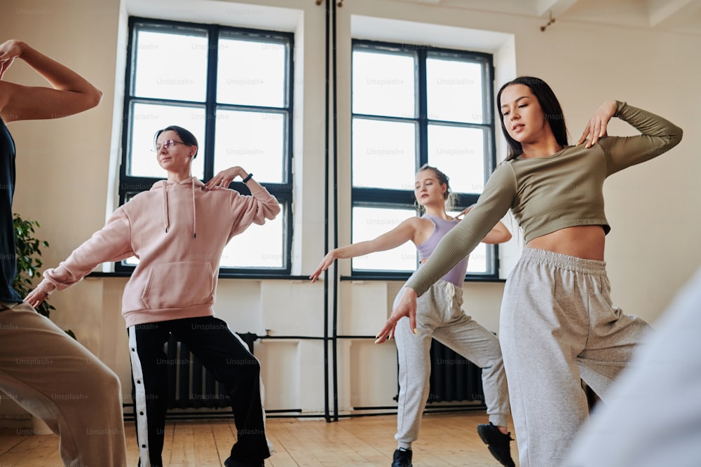 Group of contemporary active teens practicing vogue dancing movements while training in loft studio or dance hall