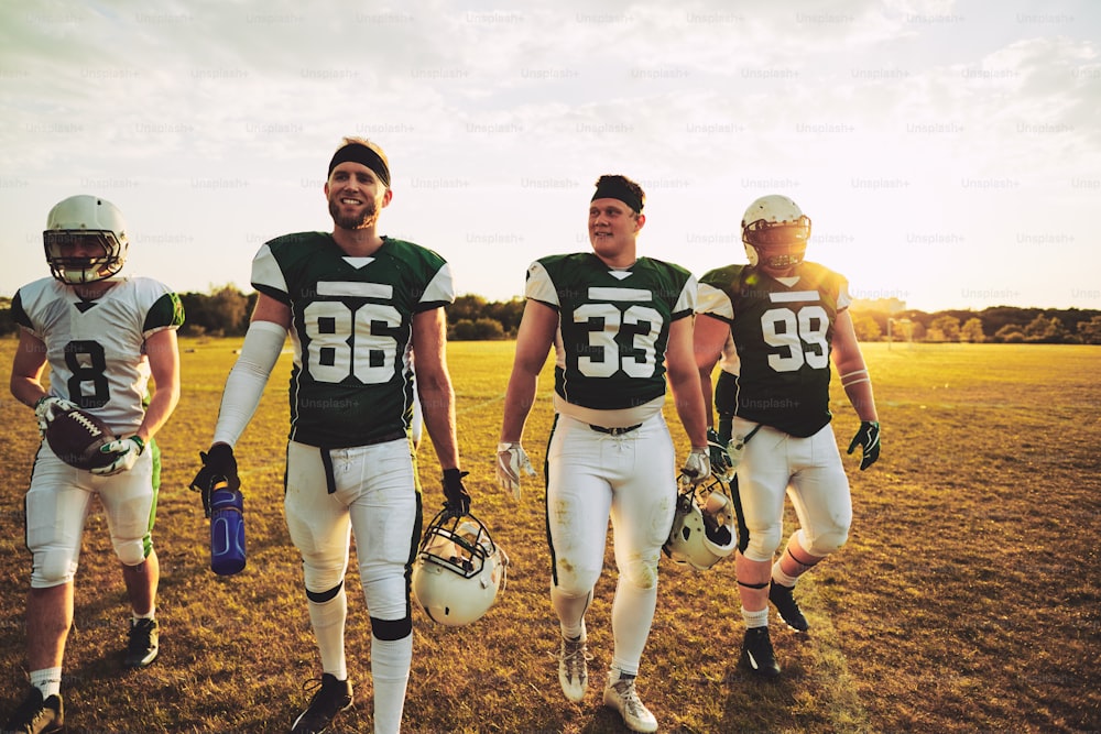 Lächelndes Team junger American-Football-Spieler, die nach einem Trainingsspiel an einem sonnigen Nachmittag gemeinsam vom Feld gehen