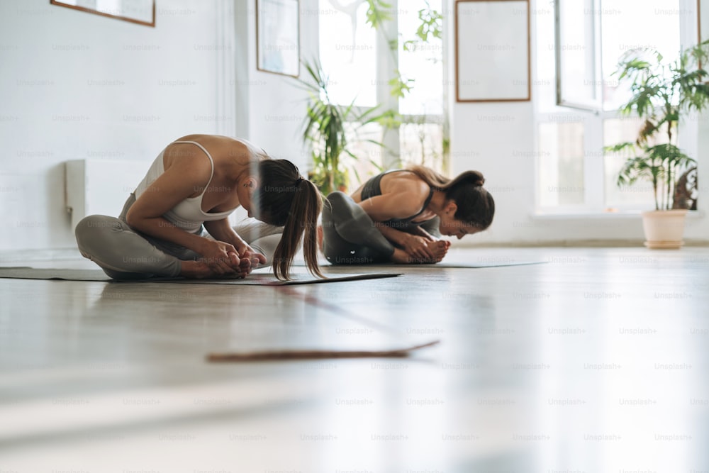 Mulheres jovens praticam yoga fazendo asana em um estúdio de yoga brilhante. Yoga ticher ajuda a fazer exercícios de asana com o aluno na aula de yoga