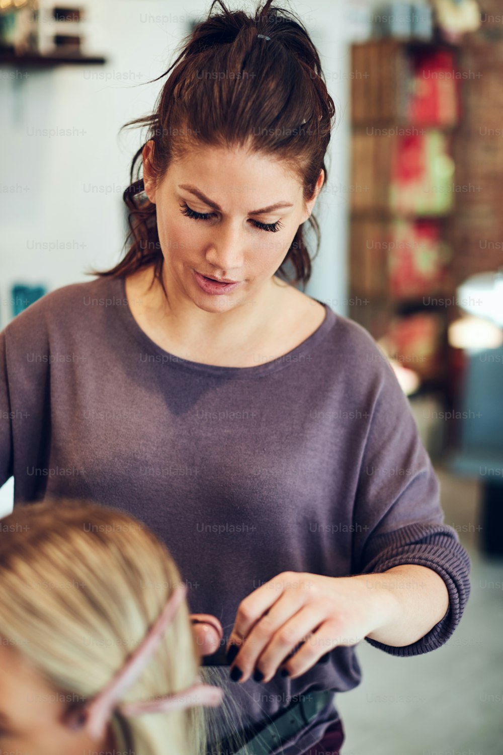 Young hairstylist using a straightener on the hair of a client sitting in a chair while working in her salon