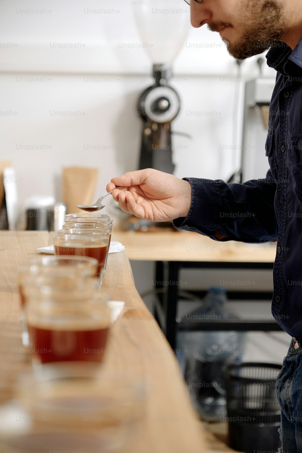 Retrato do homem degustando café recém-fabricado em xícara de vidro, usando colher, examinando o sabor e o sabor do café no teste de xícara de café para barosta
