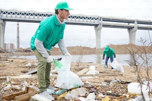 Two young men in uniform putting litter and garbage into big sacks outdoors