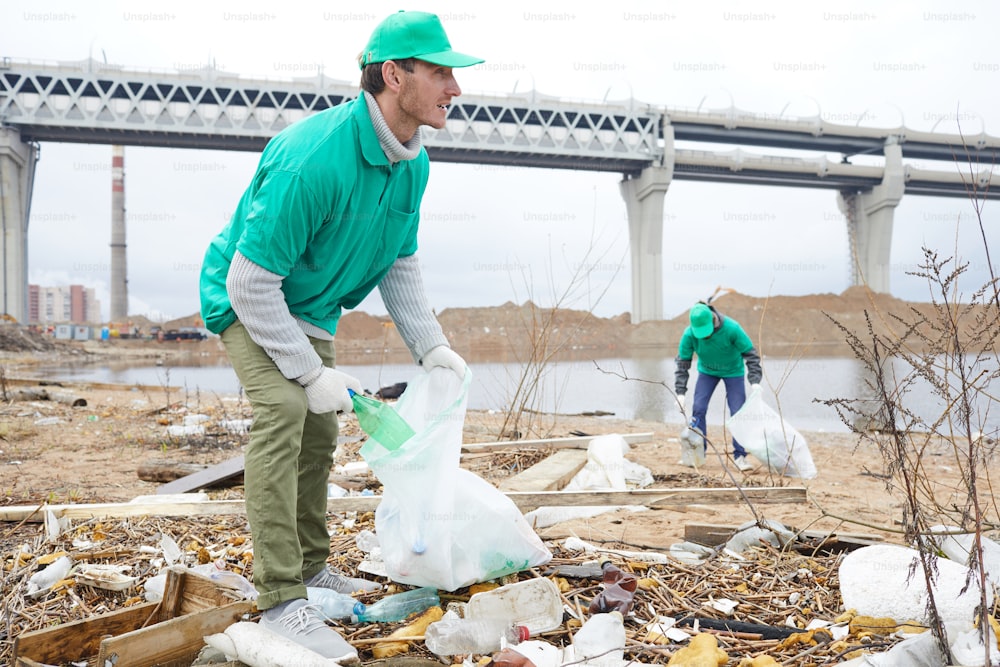 Zwei junge Männer in Uniform werfen M�üll und Müll in große Säcke im Freien