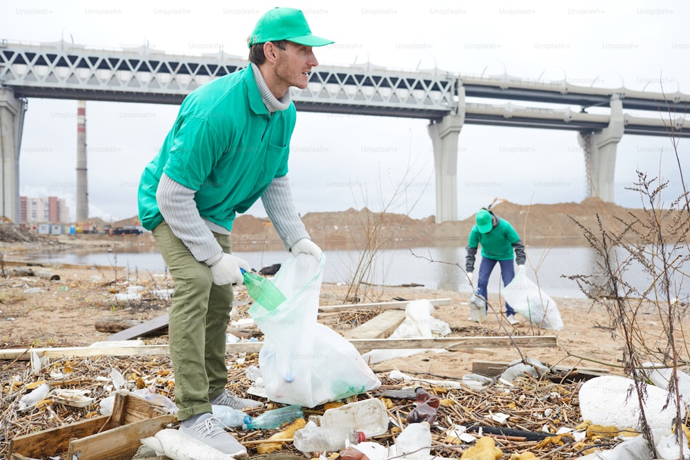 Two young men in uniform putting litter and garbage into big sacks outdoors