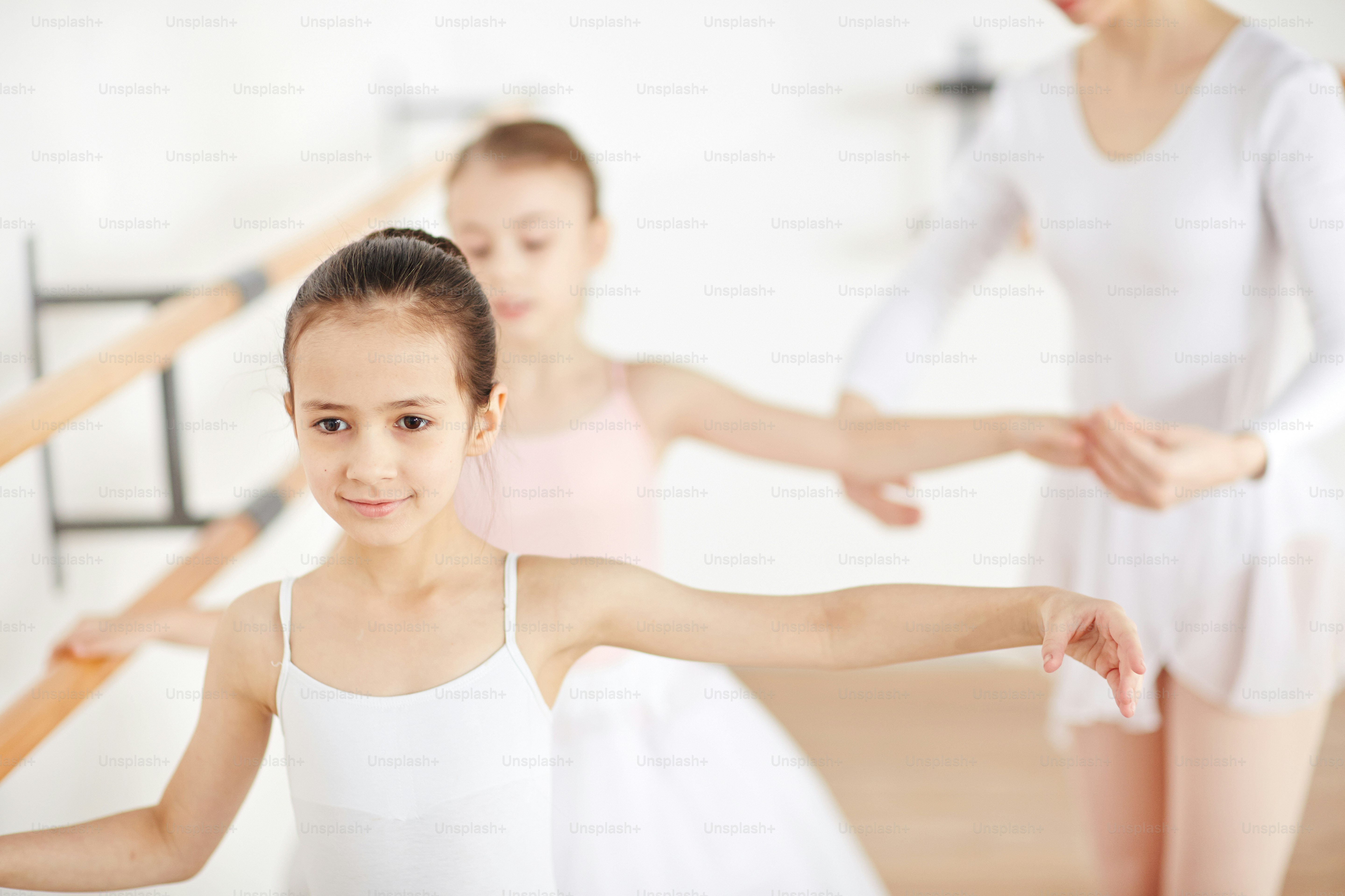 Balerina kecil yang menarik berlatih di kelas dengan bantuan guru mereka