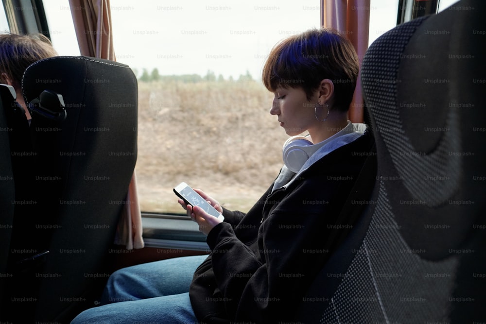 Seitenansicht eines Mädchens, das auf den Bildschirm ihres Smartphones schaut, sitzt am Fenster im Bus