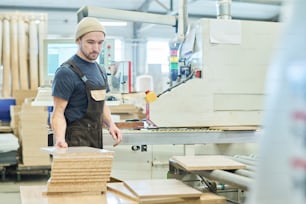 Homem jovem em geral trabalhando com madeira na fábrica em pé na máquina