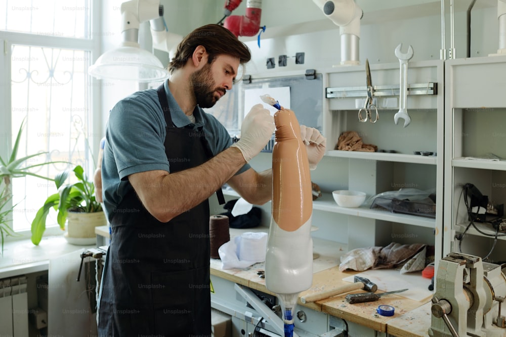 Arbeiter einer prothetischen Produktionsfabrik in Arbeitskleidung, die thermoplastische Folie auf künstliche Gliedmaßen nach Arbeitsplatz legt