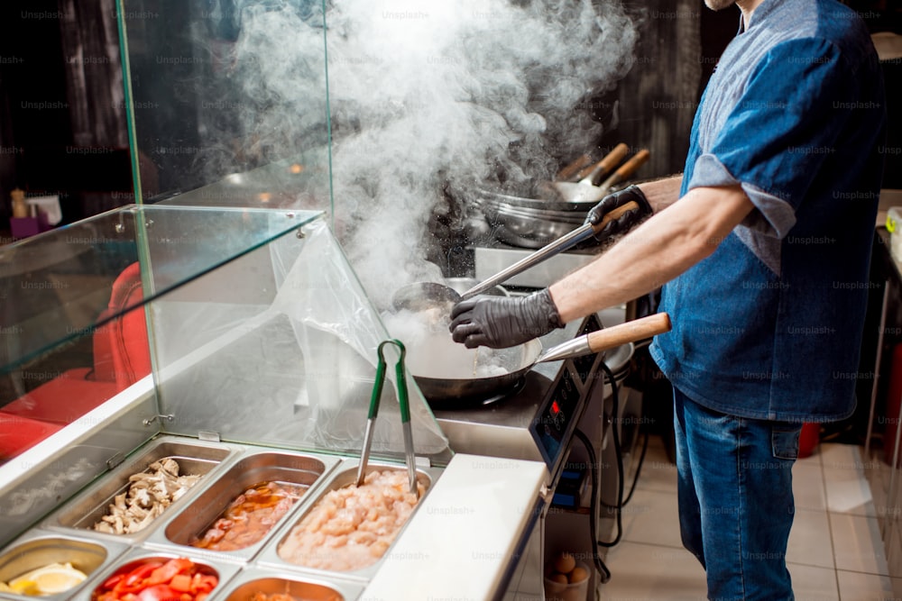 Caucasian chief cook cooking with wok pan on the asian restaurant kitchen