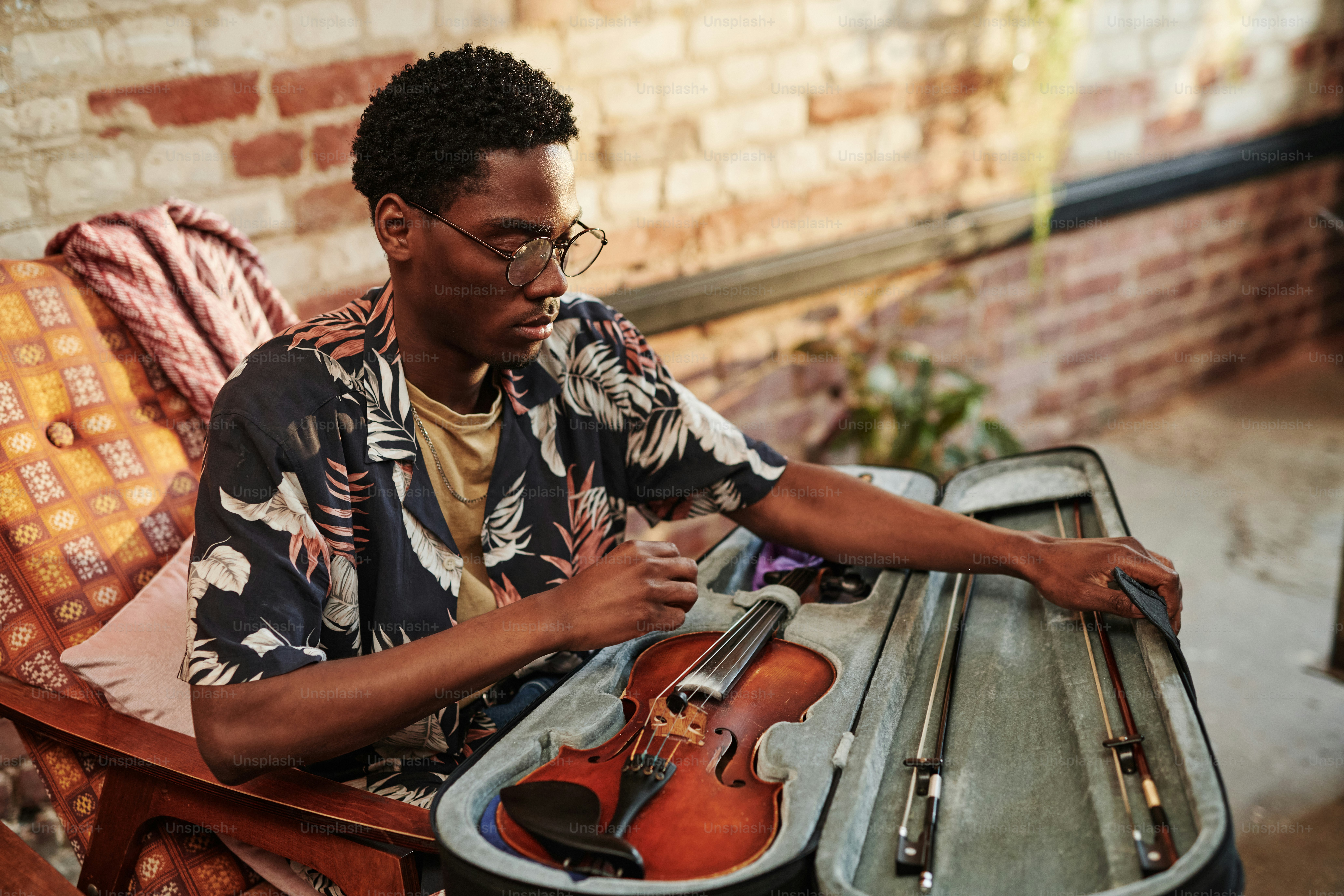 Young black man in stylish casualwear opening slipcover with violin and fiddlesticks while