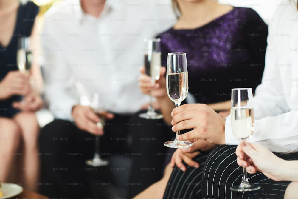 Human hands holding flutes with champagne during conversation at social gathering