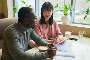 Multiethnic business couple drinking coffee and discussing financial documents at table at cafe