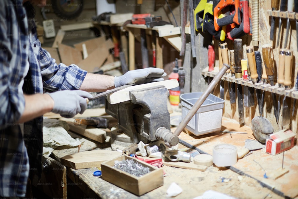 Maestro en guantes de pie junto al banco de trabajo y procesando piezas de madera en máquina mecánica