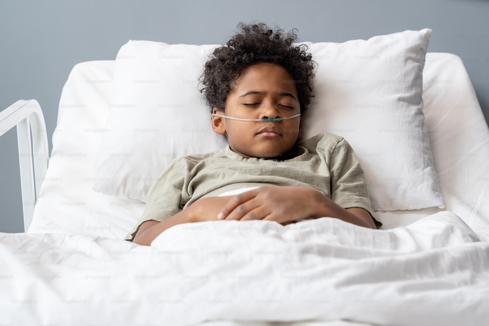 Hartkranker Junge mit Schläuchen in der Nase schläft im Bett im Krankenhaus