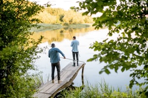 Two male friends fishing together standing on the wooden pier during the morning light on the beautiful lake