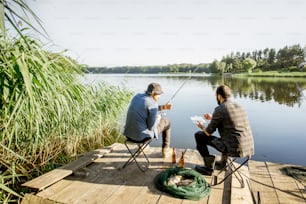 Landscape view on the beautiful lake and green reeds with two men fishing on the wooden pier during the morning light