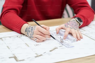 Nahaufnahme des Architekten, der den Bauplan mit Bleistift und Lineal am Tisch zeichnet