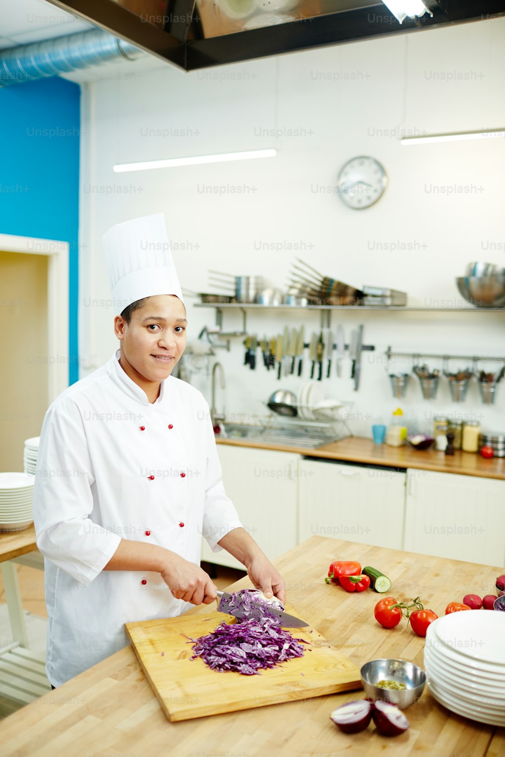 Jeune professionnel à succès en uniforme de chef coupant du chou violet frais pour la salade, la soupe ou le ragoût