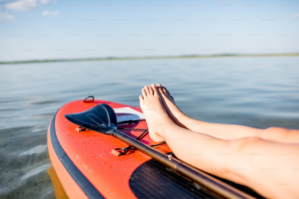 Giovane donna che si rilassa sul paddleboard sul lago. Vista ravvicinata focalizzata sulle gambe della donna
