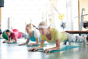 Row of active mature females doing planks on the floor in fitness center