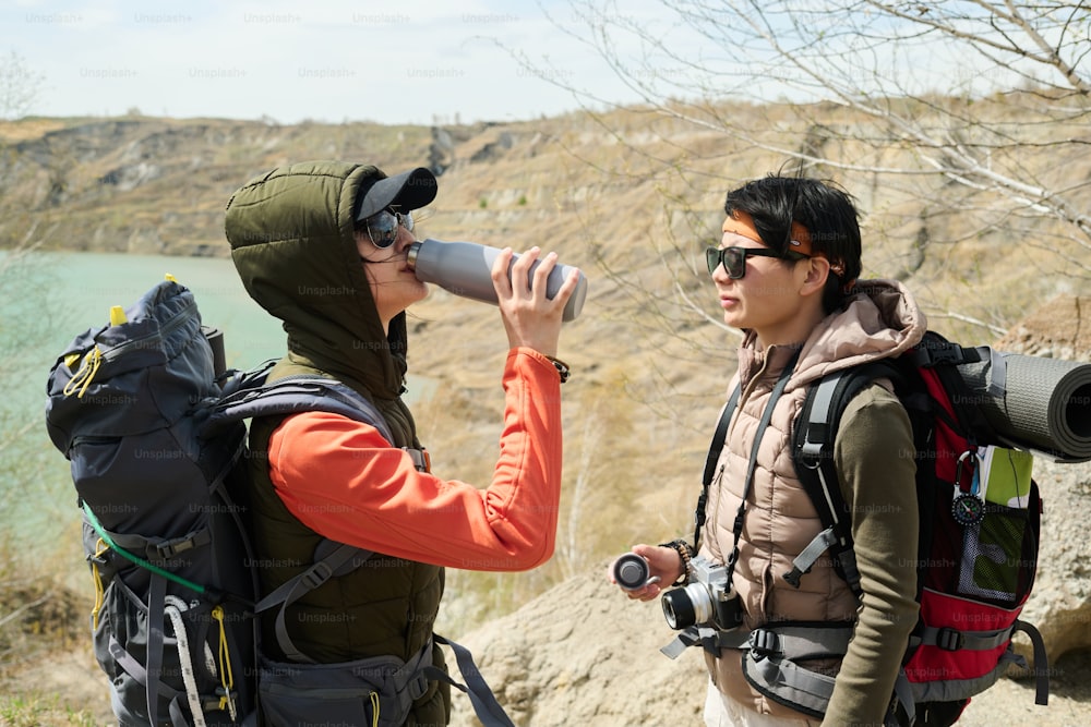 Side view of young Asian women hiking around quarry on spring day drinking tea or water from vacuum flask