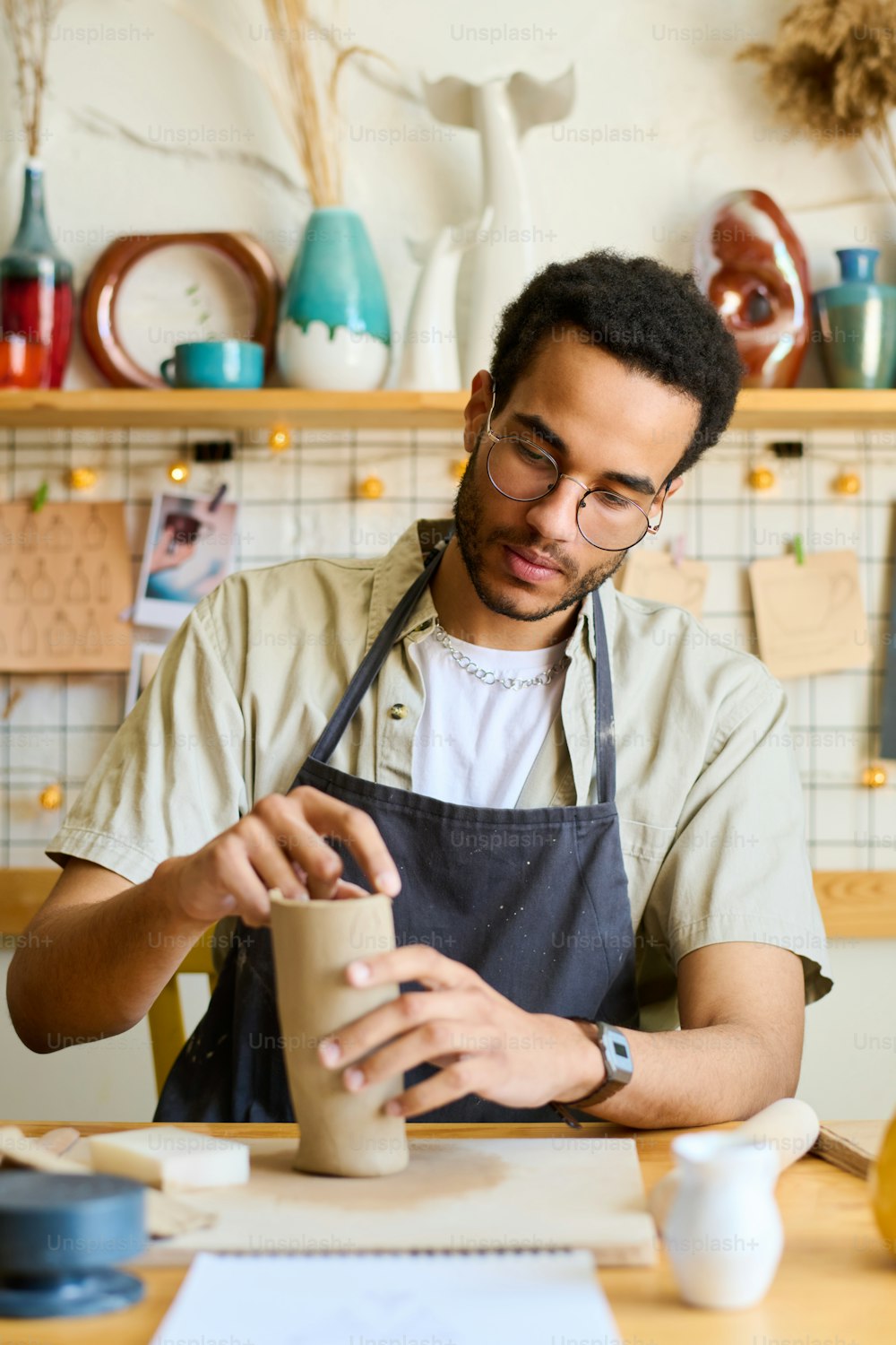 Creative male pitcher making new clay vase or jug while sitting by table with supplies for creatibe earthenware in studio or workshop