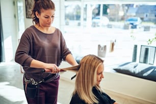 Young blonde woman sitting in a salon chair getting her long blonde hair straightened by her hairstylist