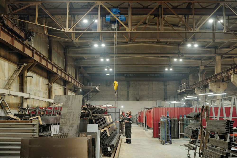 Interior of spacious factory workshop where male engineer adjusting industrial machine or other construction equipment
