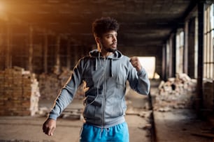 Ritratto ravvicinato di giovane afroamericano attivo attraente uomo atletico che fa allenamento di stretching a mano intera all'interno del luogo abbandonato.