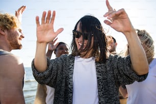 Bel homme asiatique portant des lunettes de soleil dansant entre amis tout en s’amusant lors d’une fête multiethnique sur la plage.