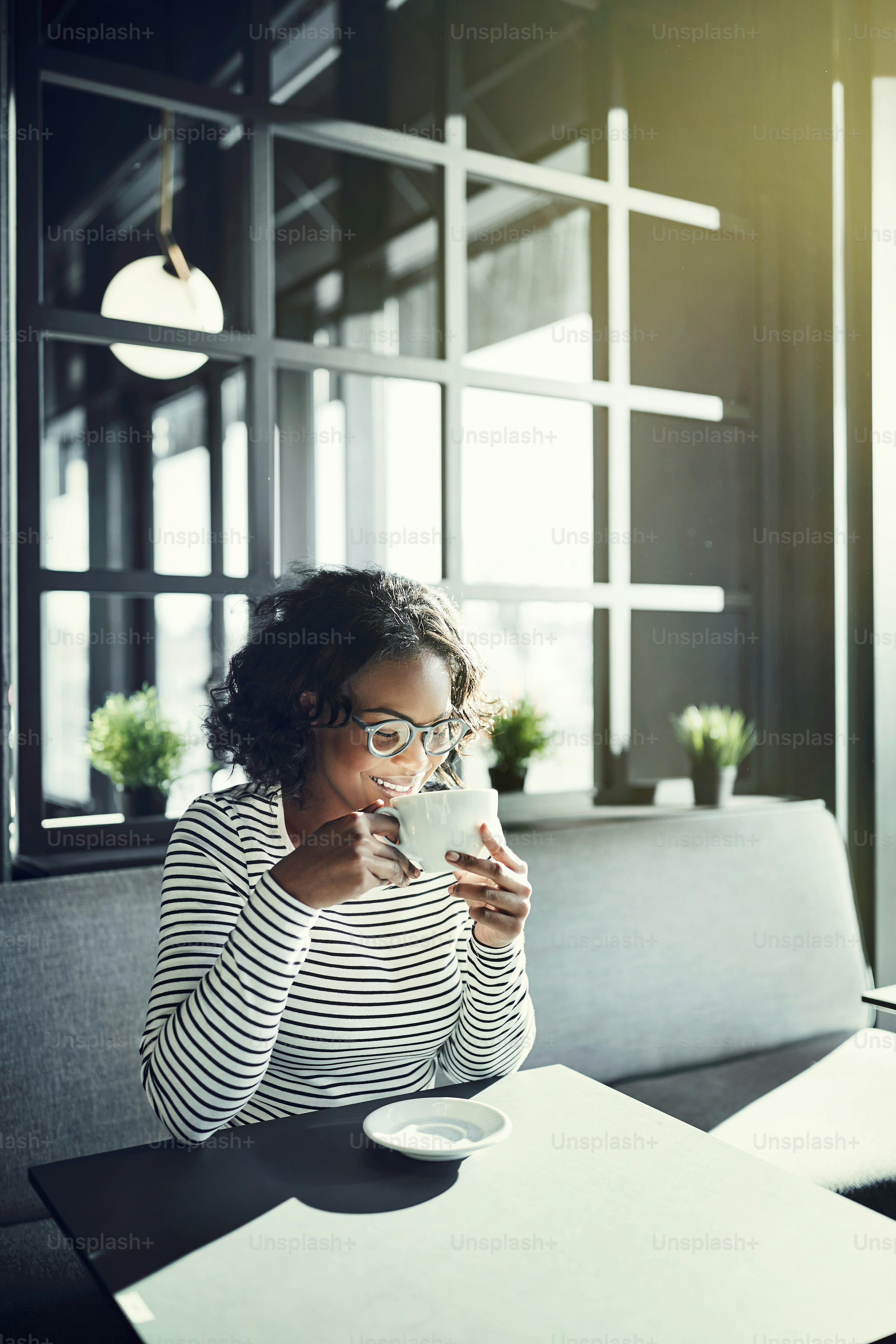 Smiling young African woman sitting with her eyes closed at a table in a cafe enjoying the aroma of her fresh cup of coffee