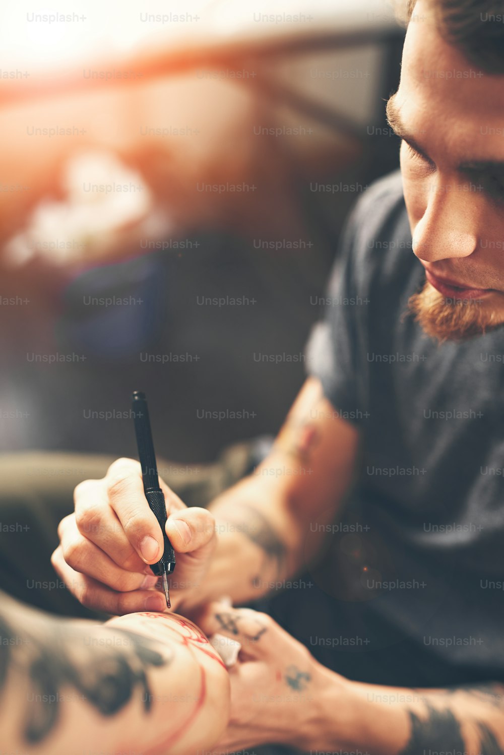 A young guy, a tattoo artist preparing for the session, draws a sketch on the body of the client in a welcoming environment