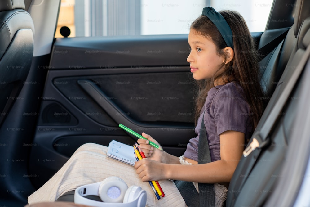 Menina bonita com lápis de cera esperando pais enquanto sentado no banco de trás do carro