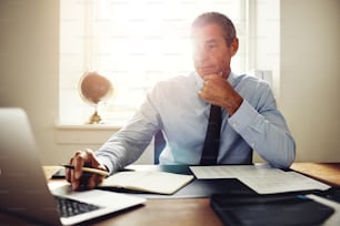Empresário maduro vestindo uma camisa e gravata sentado em sua mesa de escritório trabalhando on-line com um laptop
